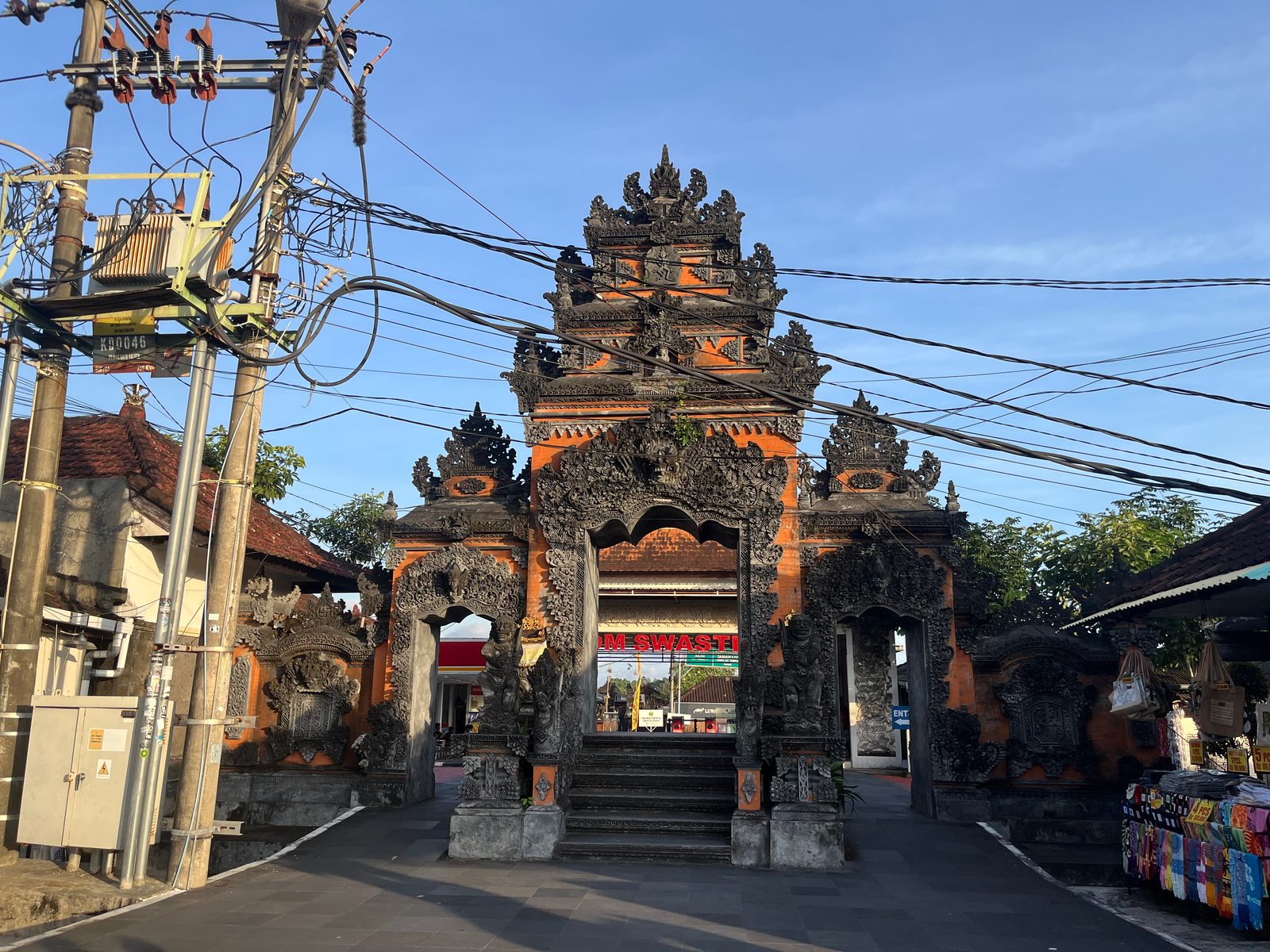 A carved Balinese temple gate crossed by a tangle of overhead cables, with a transformer pole on the left