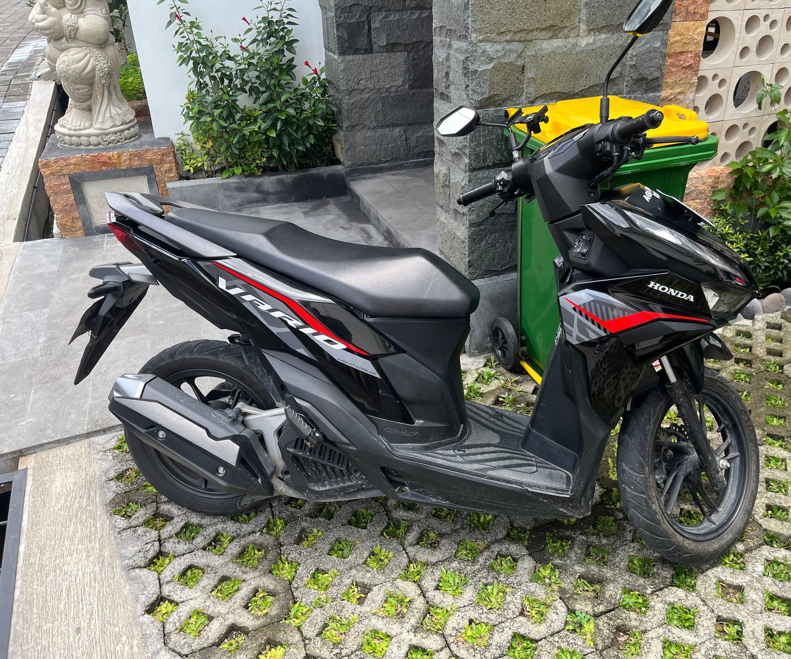 A black Honda Vario scooter parked on a paved driveway