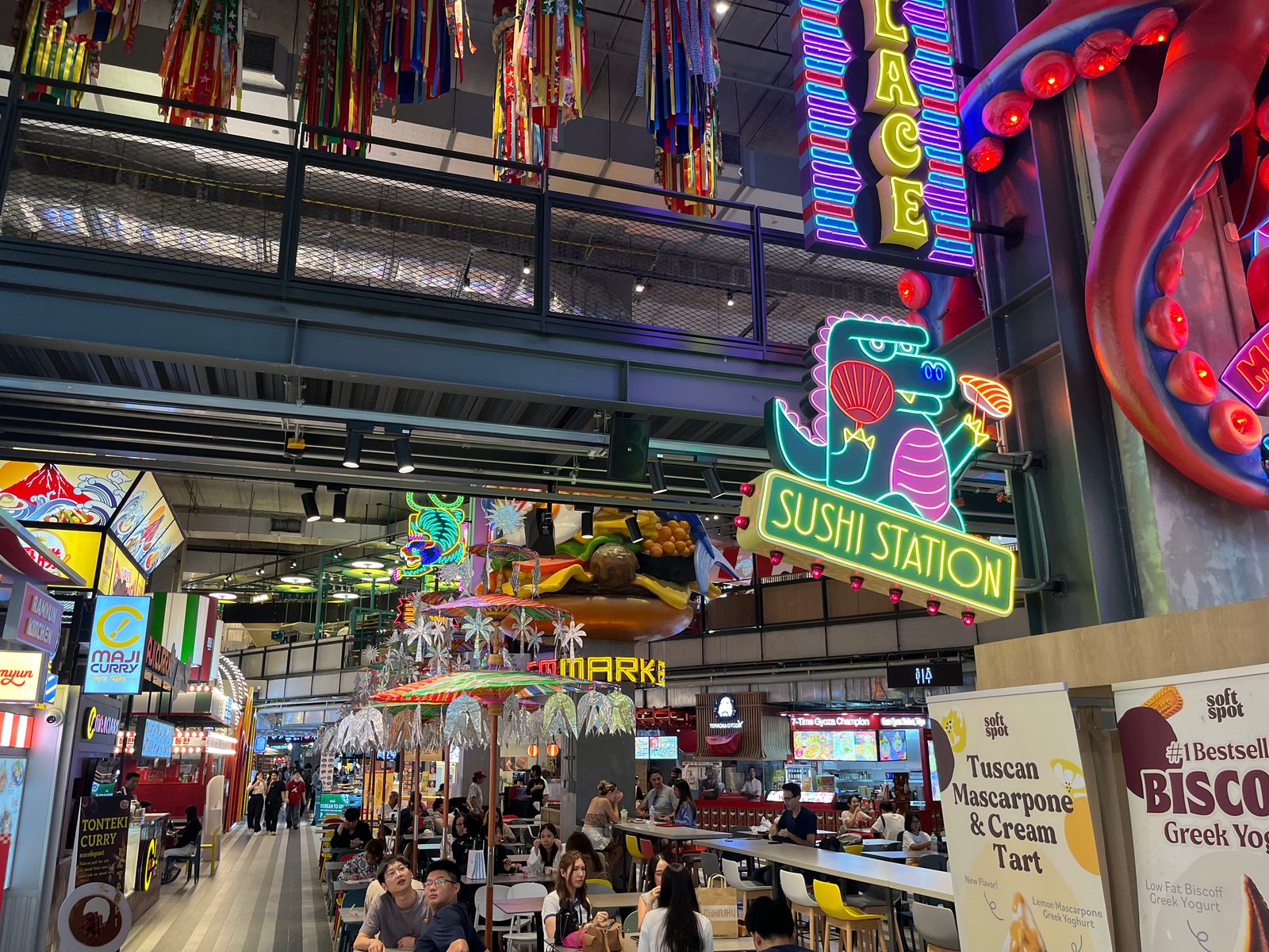 Neon signs, including a sushi dinosaur, over the busy food hall at EmSphere