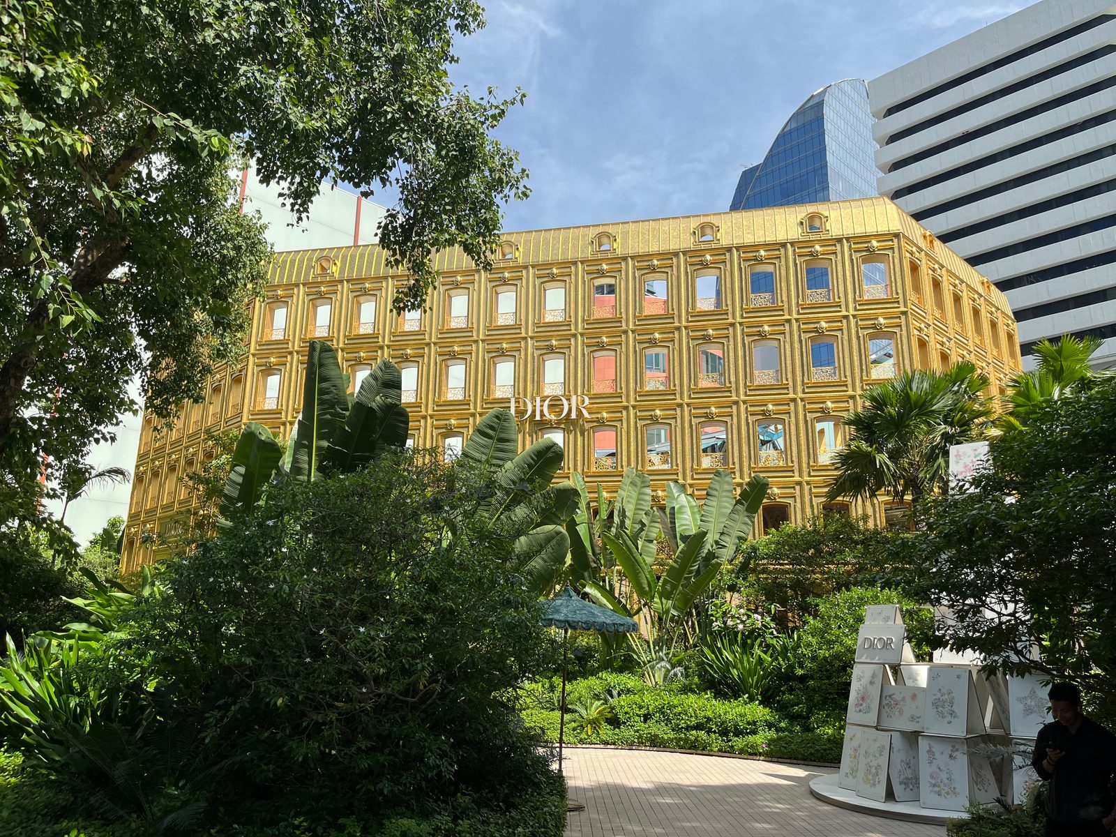 A gold-clad Dior building behind tropical plants under a blue sky