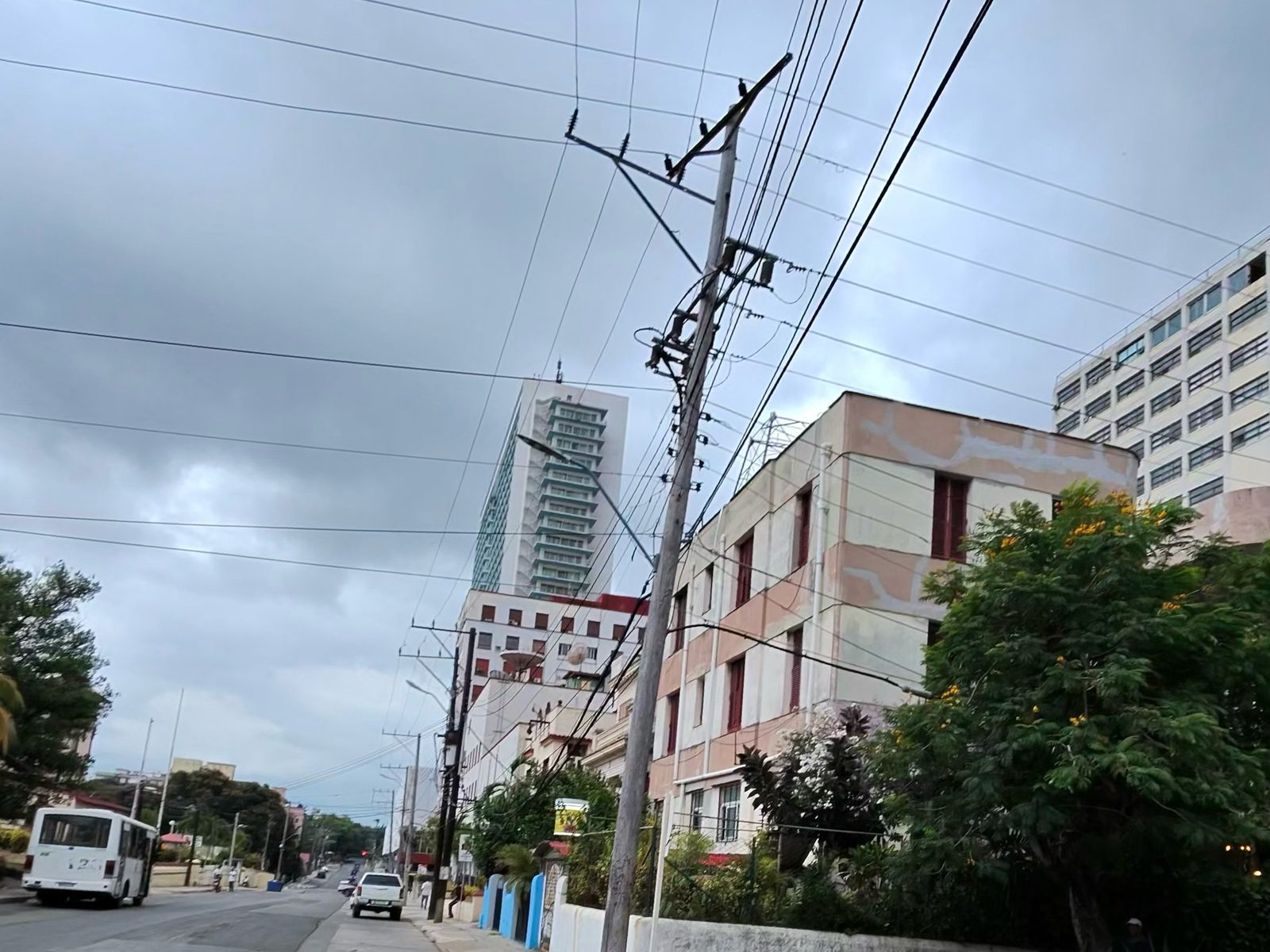A utility pole carrying a dense bundle of overhead cables on a Vedado street corner under a cloudy sky