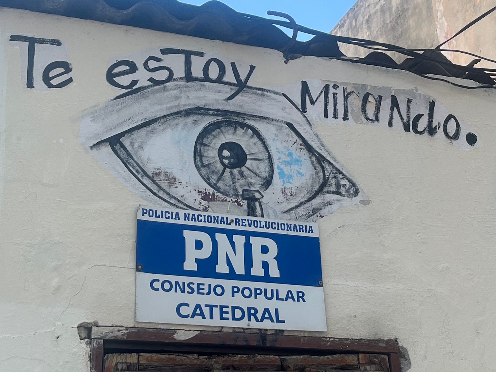 A PNR police sign for the Catedral district below a painted eye and the words “Te estoy mirando”