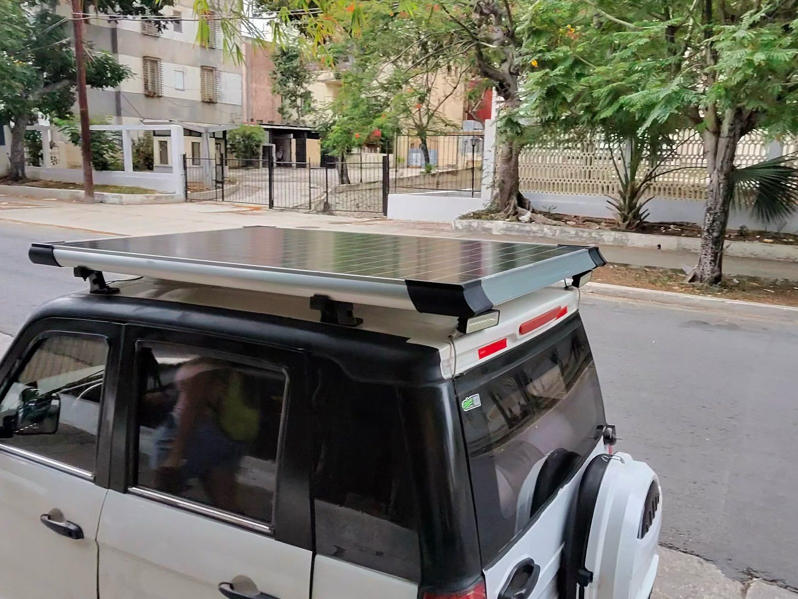A small car with a solar panel on its roof rack, parked on a Vedado street