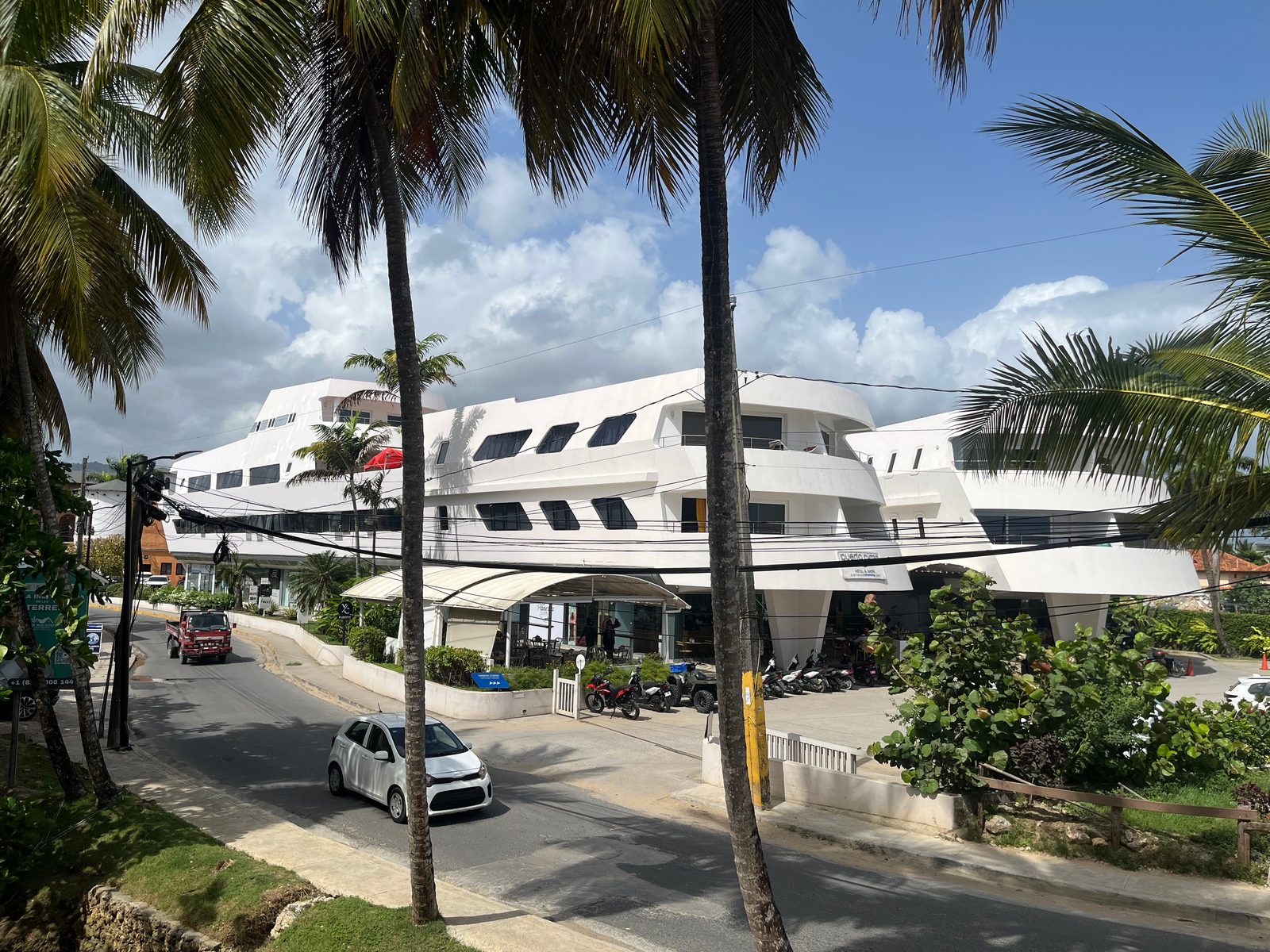 White low-rise apartment complex among palm trees beside a quiet road