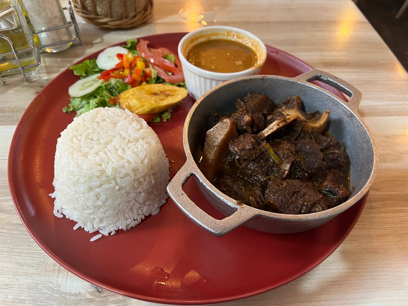 Dominican lunch plate with white rice, stewed meat in a small pot, beans in a cup, salad and tostones