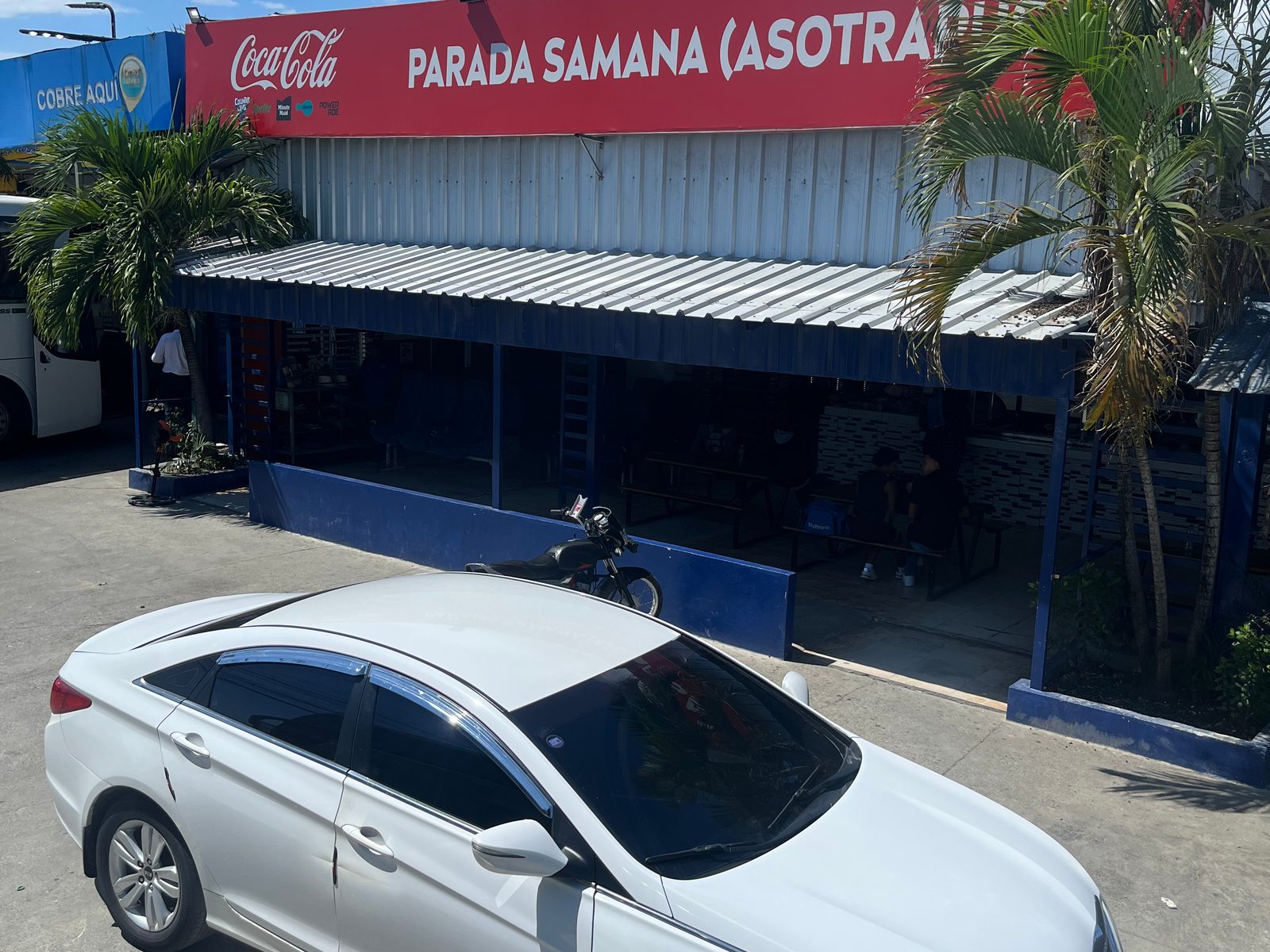 Bus stop with a red sign reading Parada Samaná (Asotrapusa) and a white car parked in front