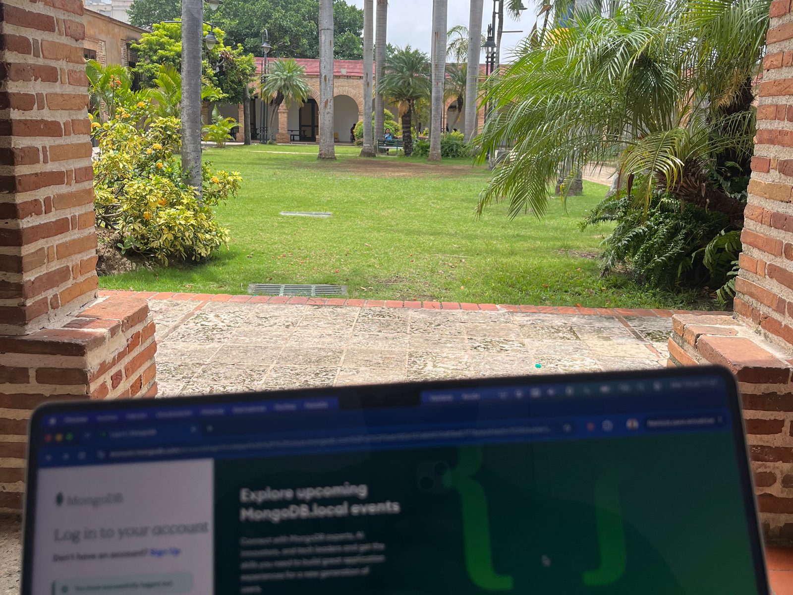 Laptop open on a brick ledge under an arch, looking onto the palm-lined lawn of the Ozama Fortress