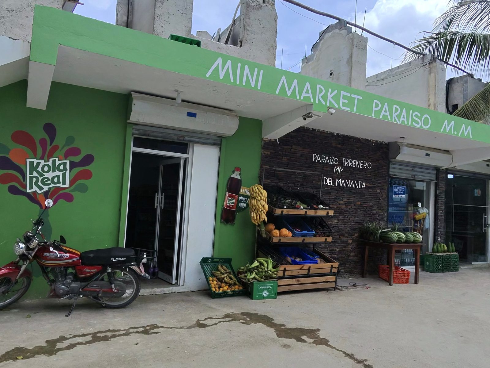 Green corner shop called Mini Market Paraíso with fruit crates by the door and a motorbike parked outside