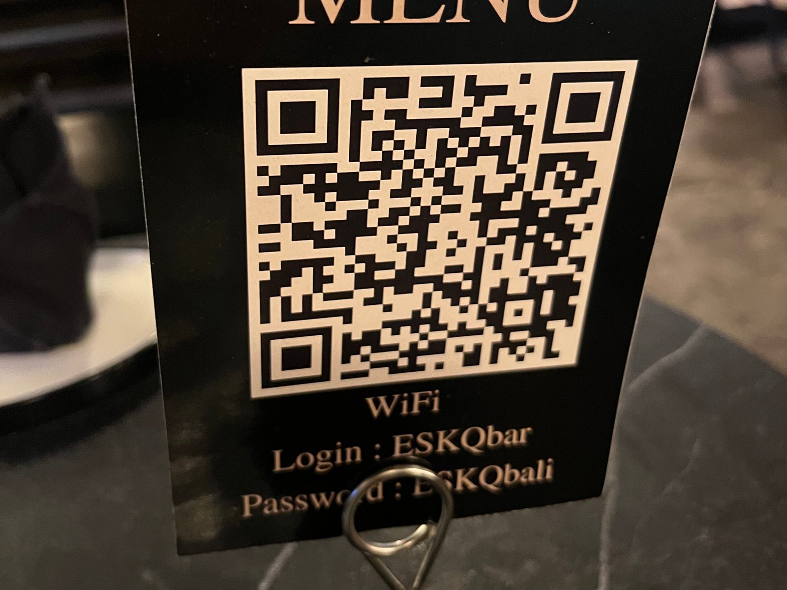 A menu stand with a QR code and the venue’s wifi login and password on a dark bar table