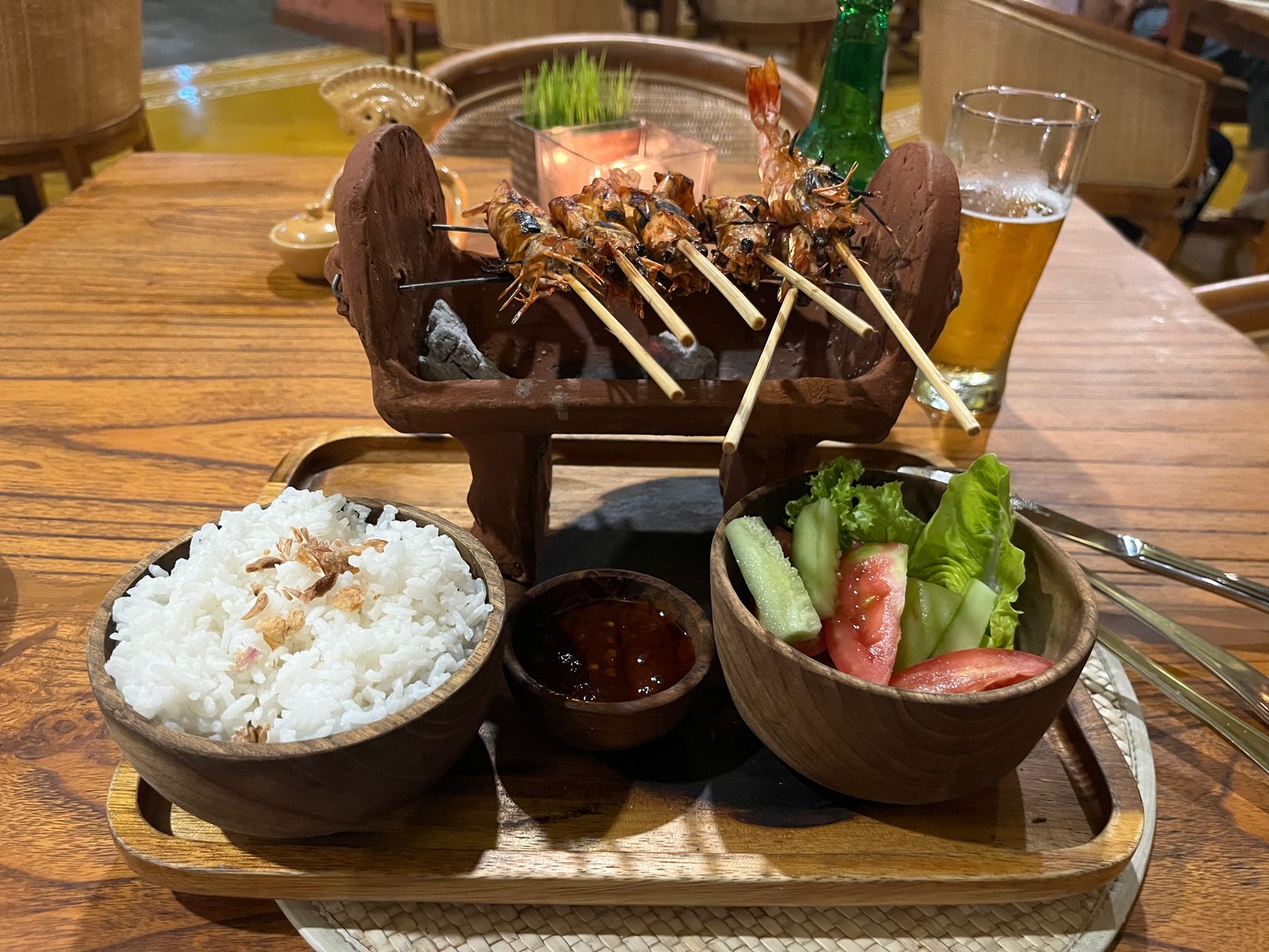 Satay skewers on a small wooden grill served with rice, sambal and vegetables