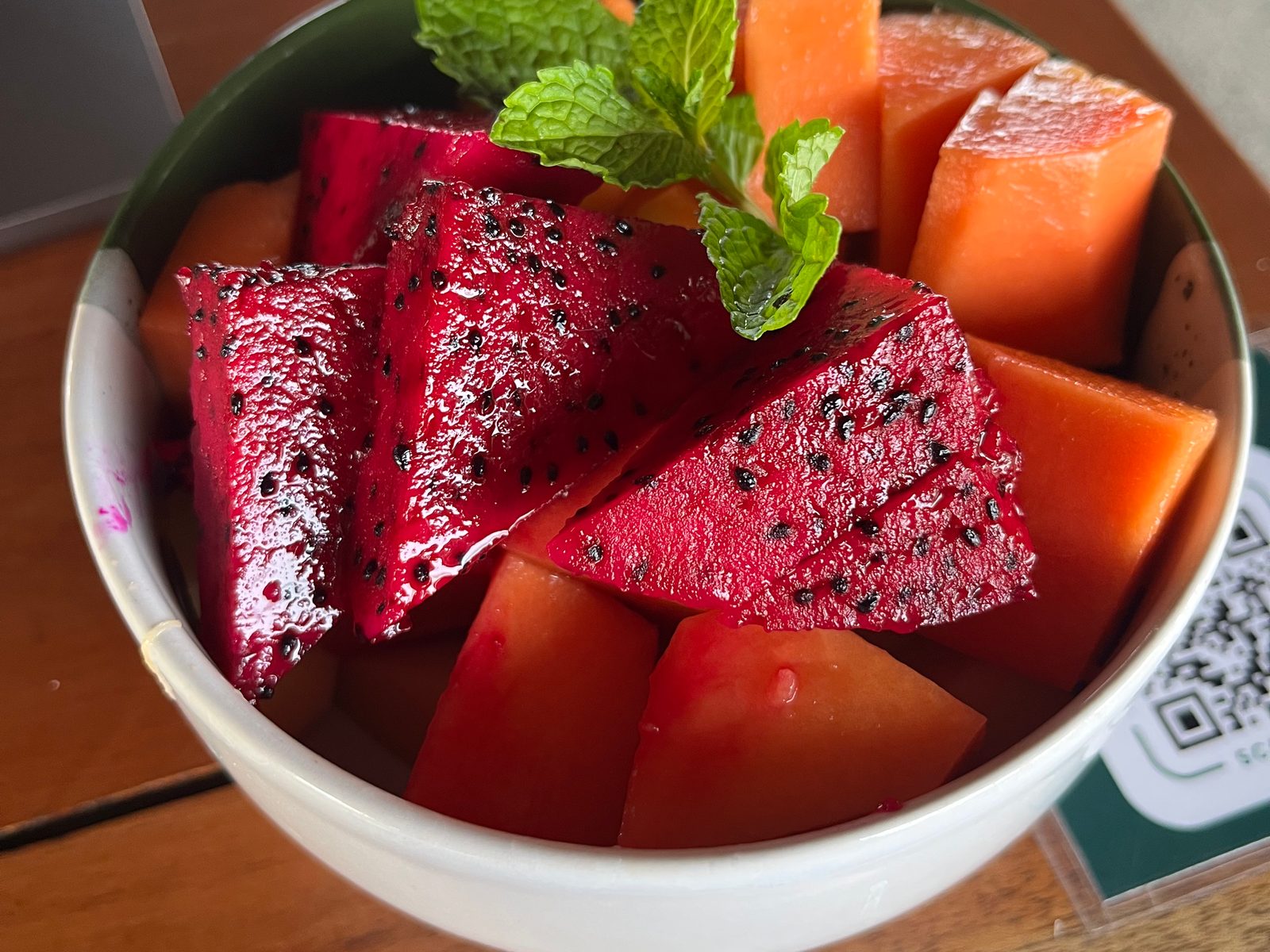 A bowl of cut red dragon fruit and other tropical fruit topped with mint