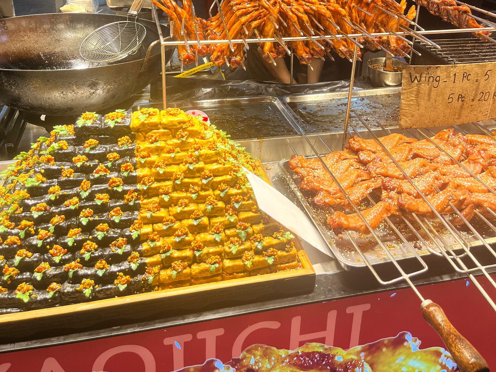 Grill stall on Jalan Alor with chicken skewers, trays of wings and a handwritten price card