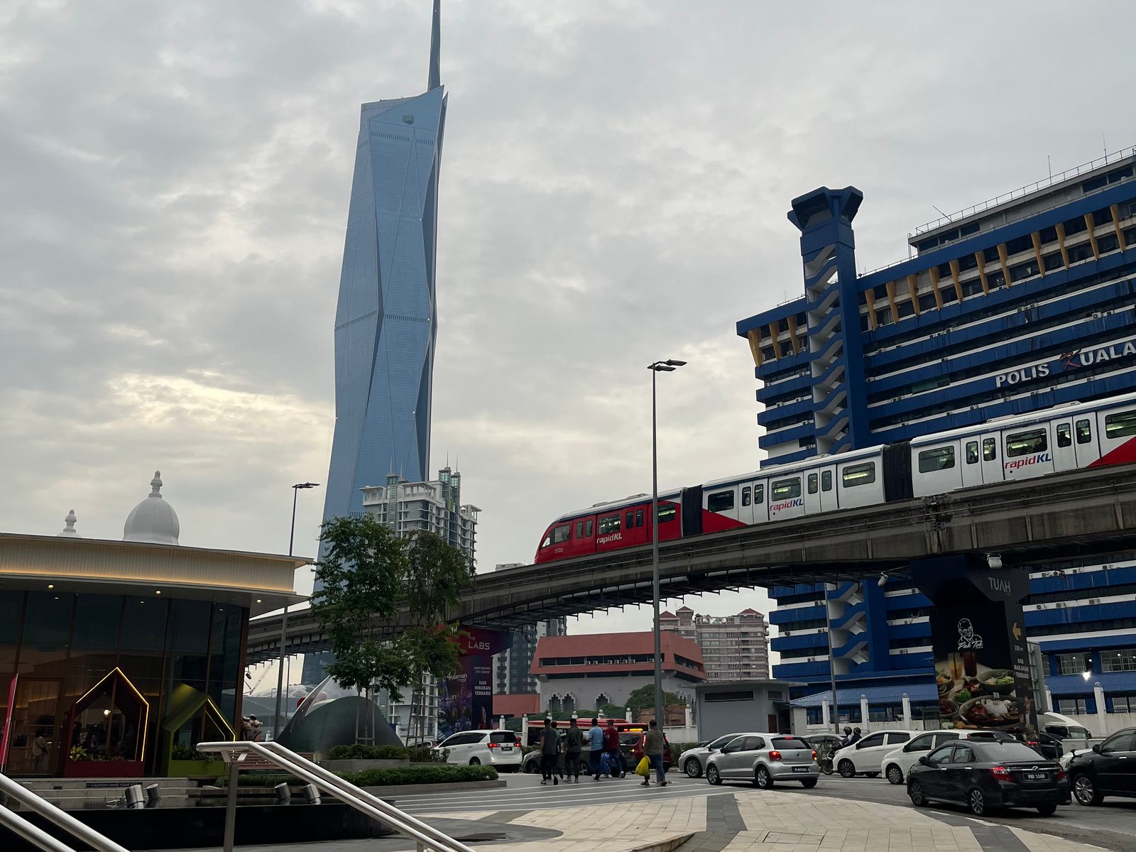 A red KL Monorail train on its elevated track with the Merdeka 118 tower behind