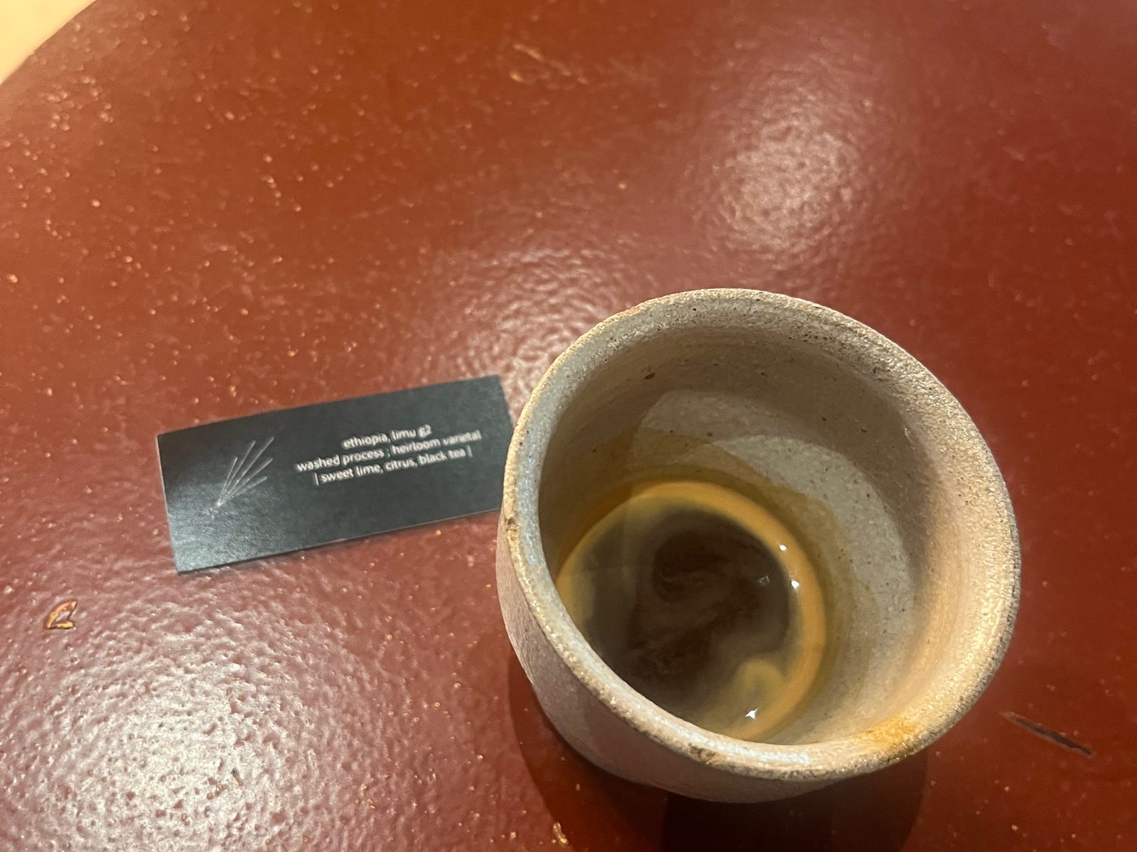 A cup of filter coffee next to a small tasting card on a café table in Kuala Lumpur