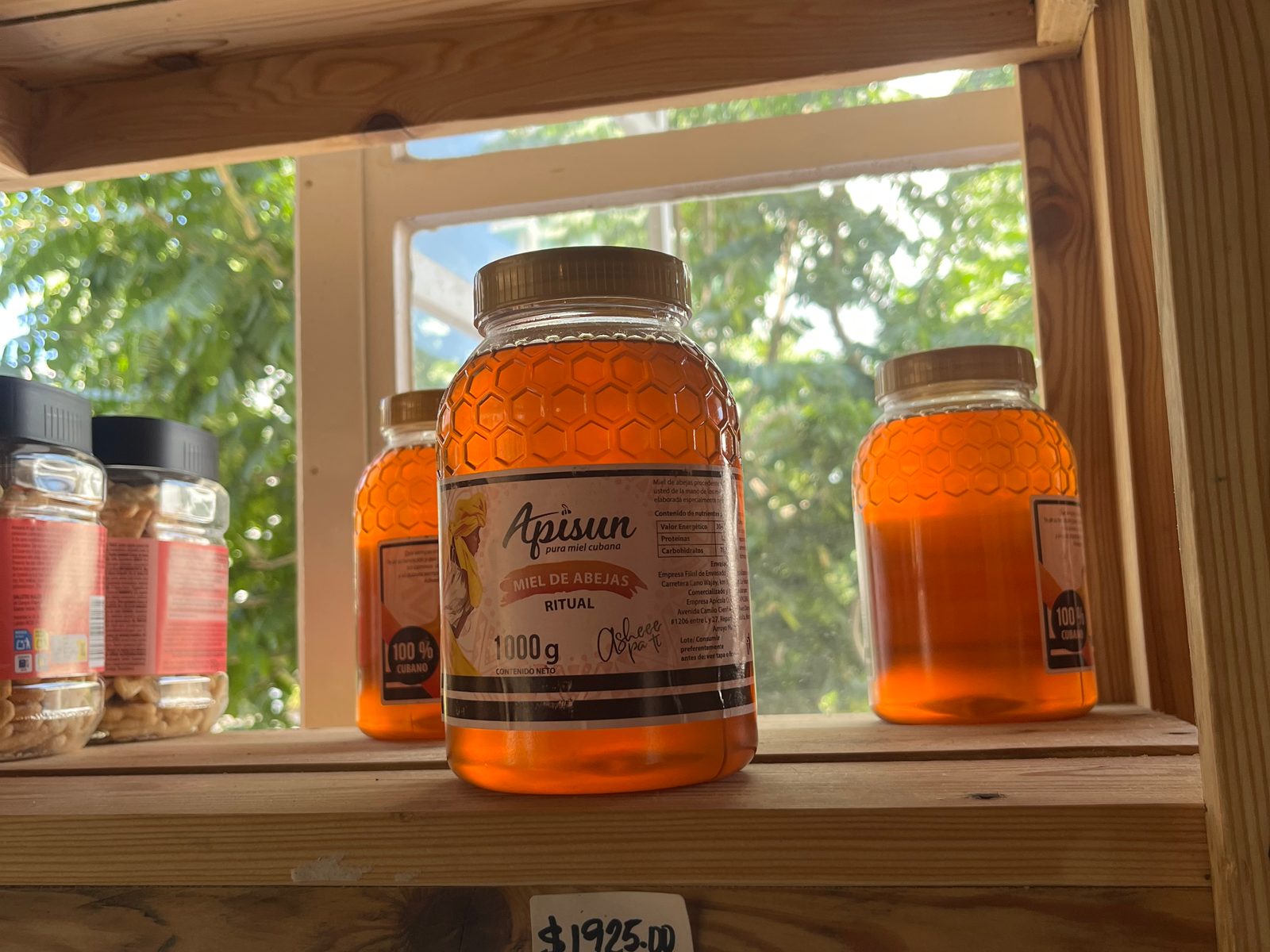 Jars of honey on a wooden shop shelf with a handwritten peso price tag