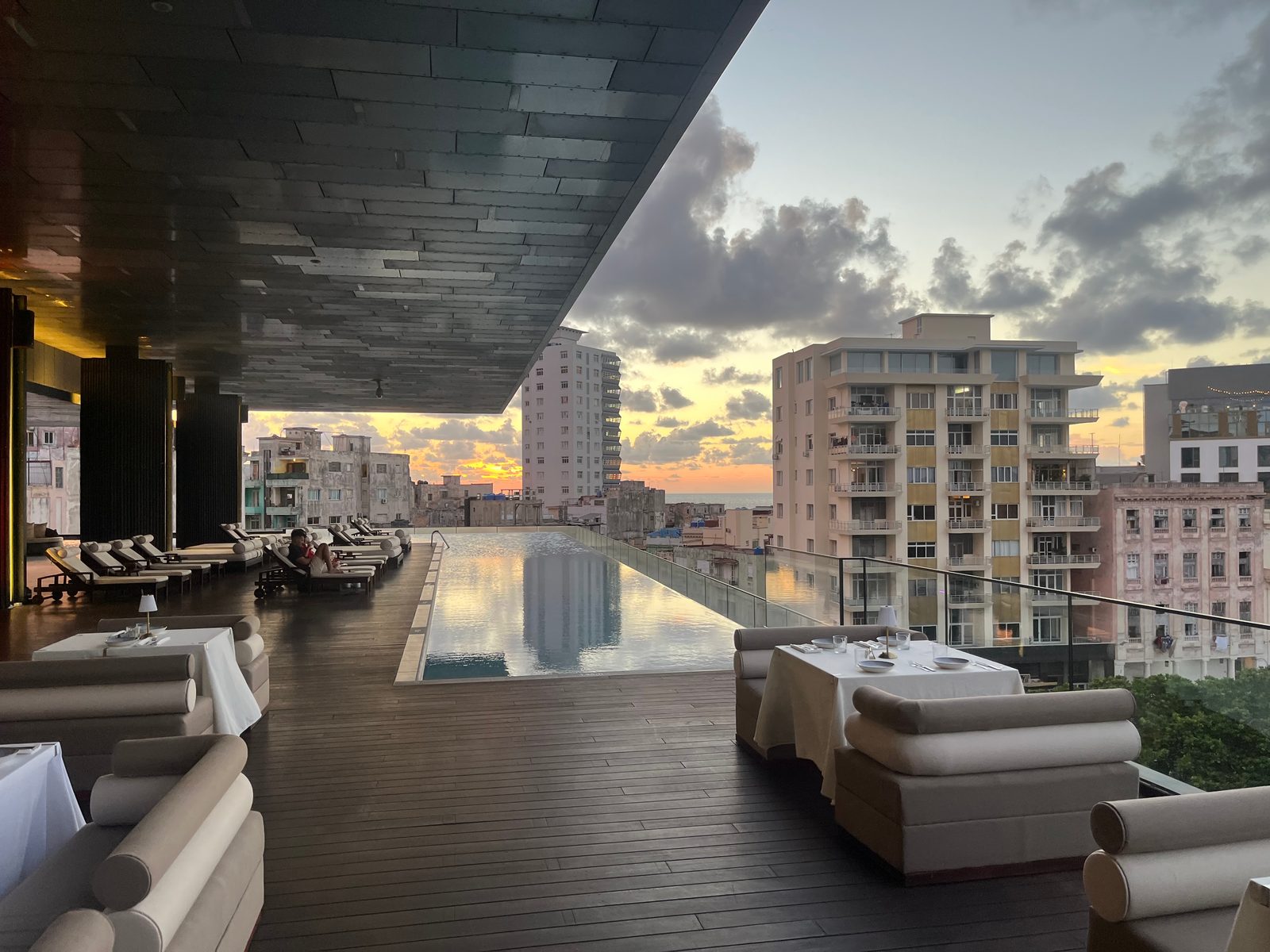 A hotel rooftop terrace with an infinity pool and lounge seating above Havana at dusk