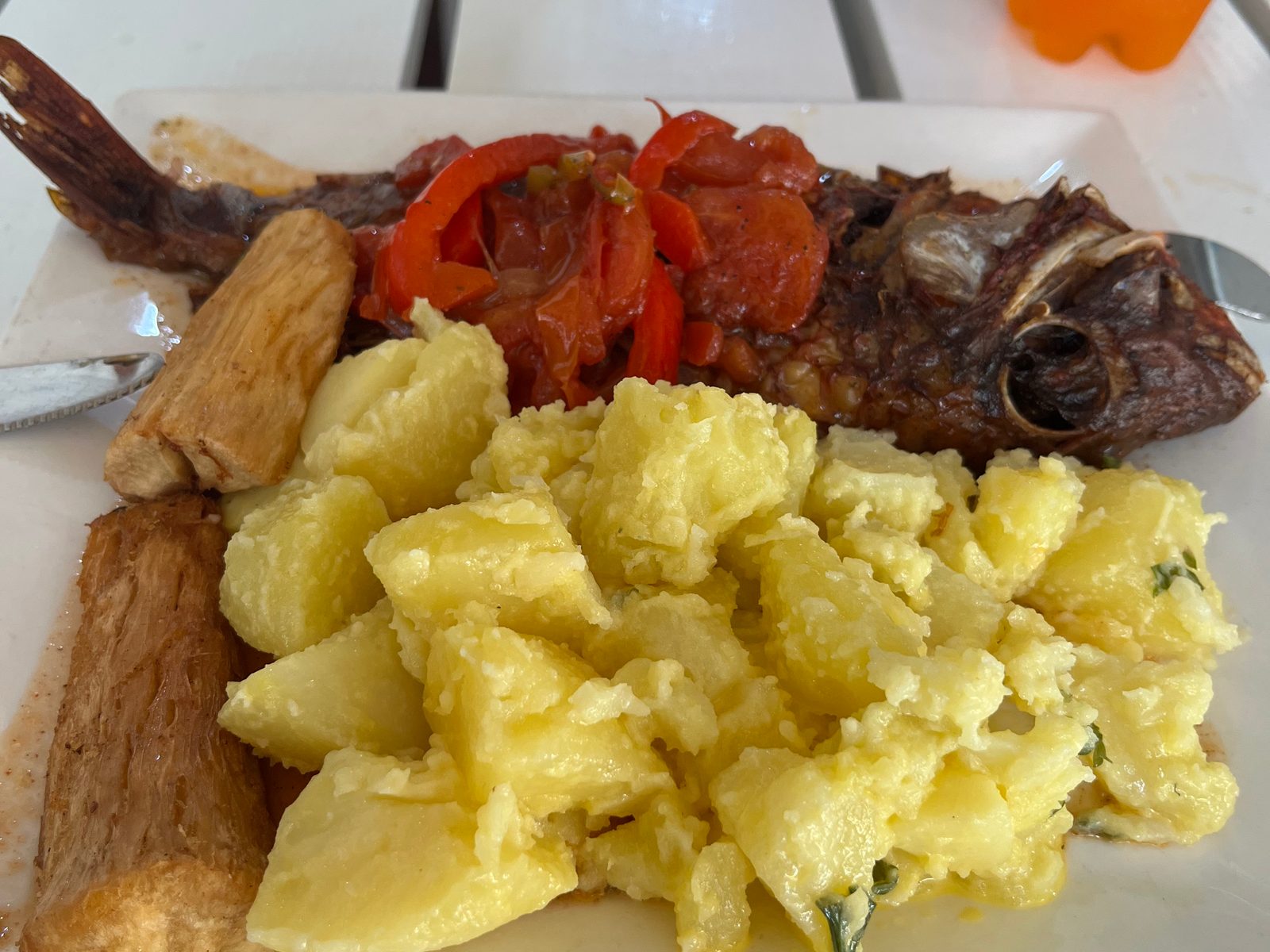 Whole fried fish topped with tomato and pepper, potato salad and yuca on a white plate