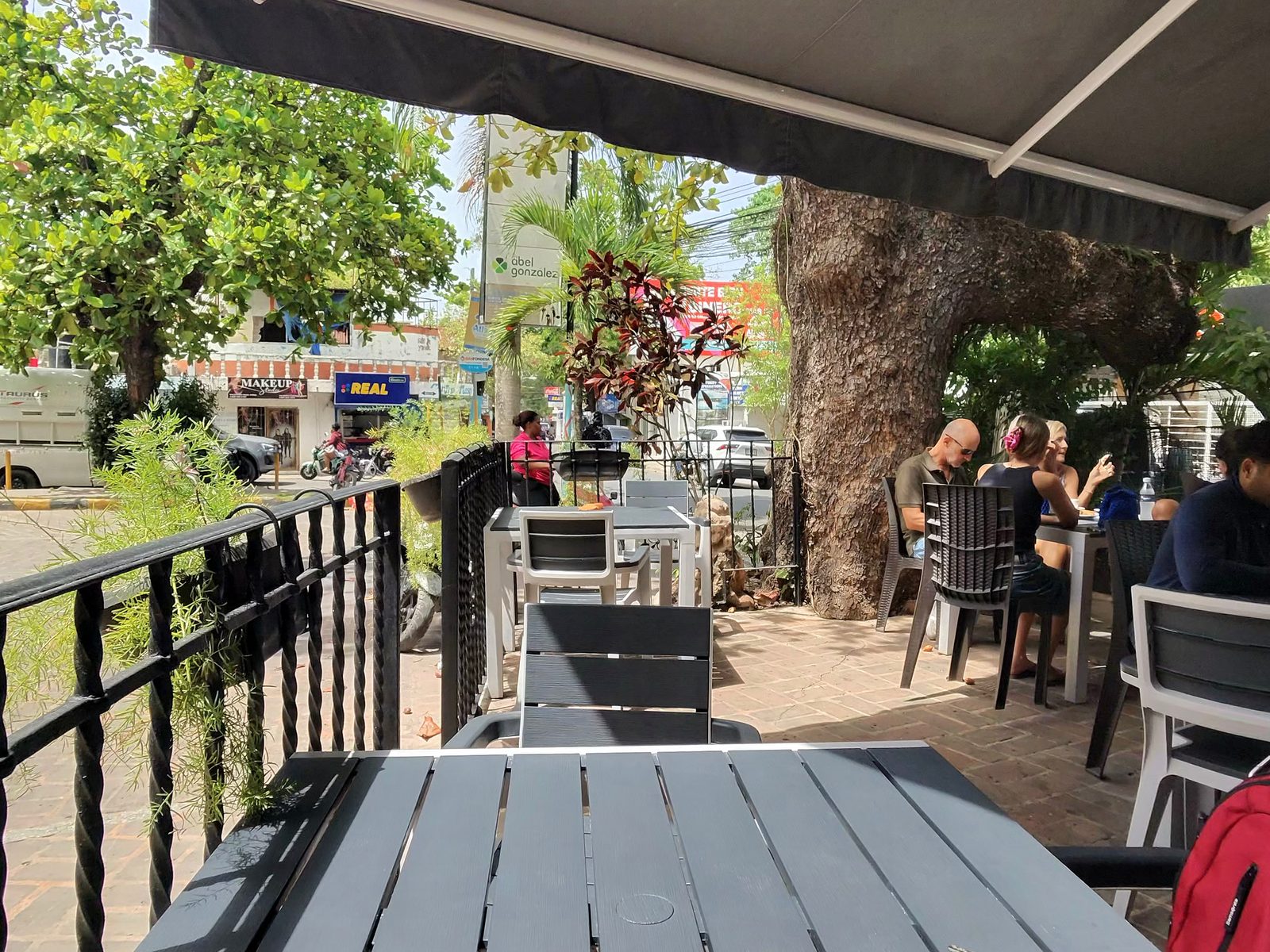 Espresso cup on a café table under an awning, with a big tree and other tables behind