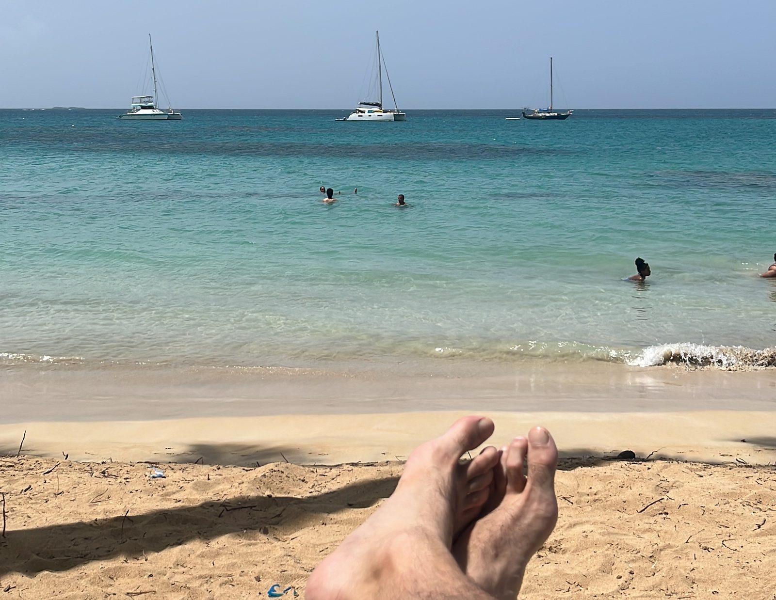 View from a sunbed at Punta Popy: turquoise water, swimmers and sailboats offshore