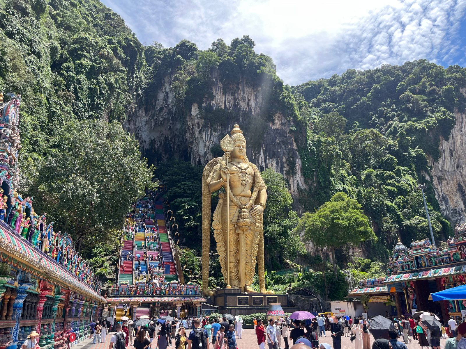 The golden Murugan statue and colourful stairs at Batu Caves under a limestone cliff