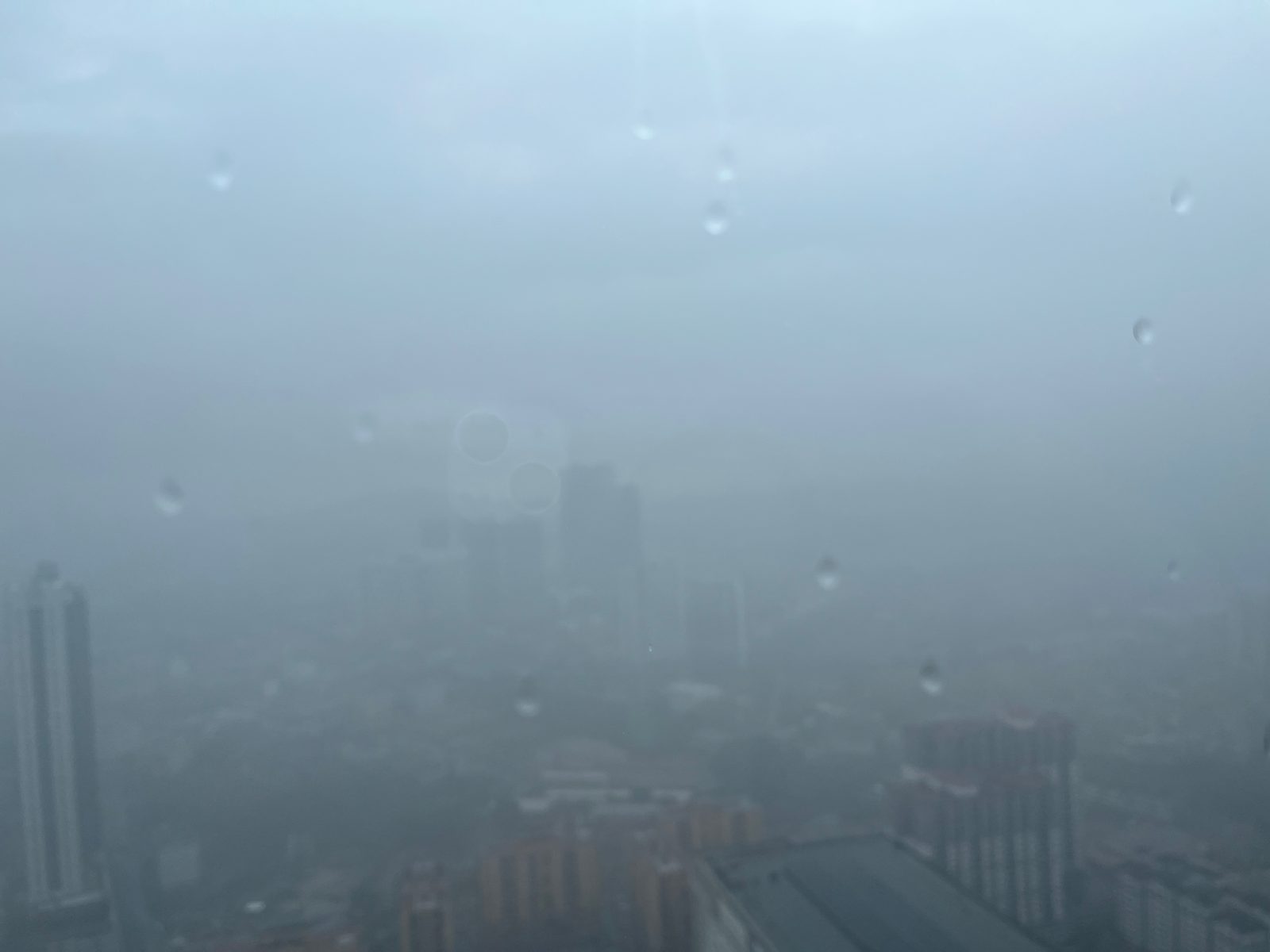 Kuala Lumpur skyline almost hidden by a rainstorm, seen through a wet window