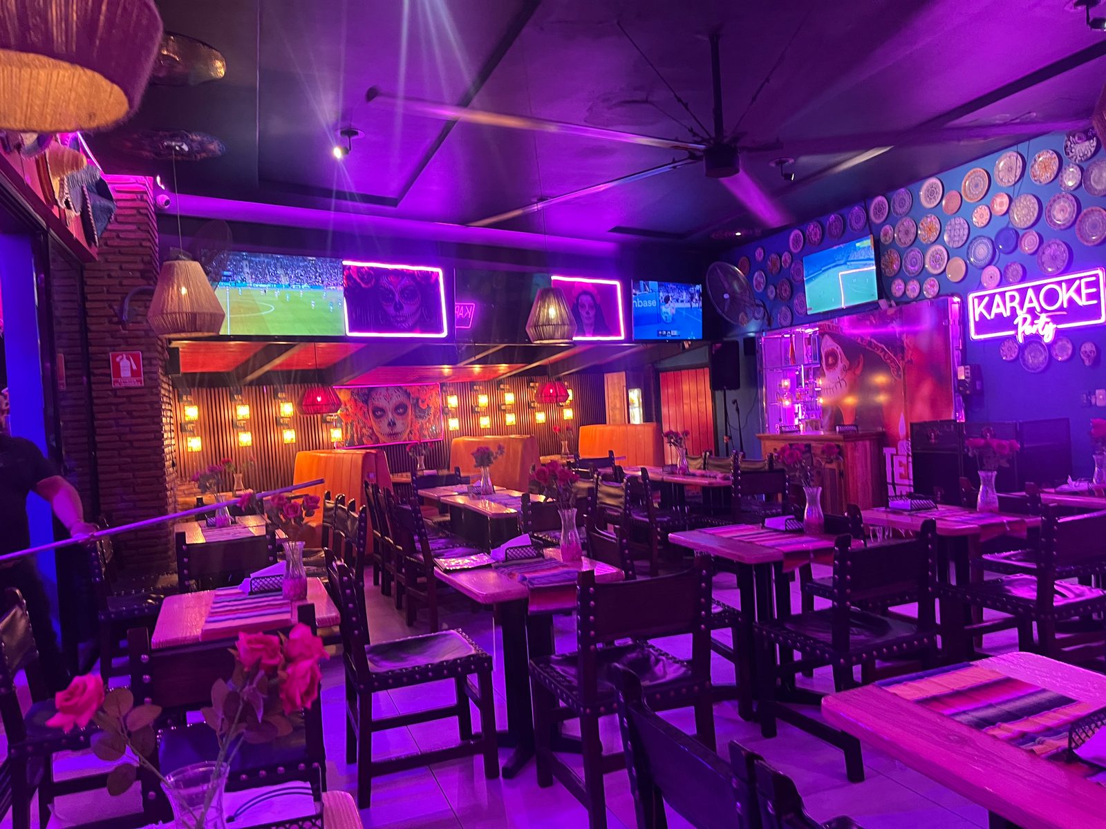 Restaurant lit in purple and pink neon, with wooden tables, sports on TV screens and a karaoke sign