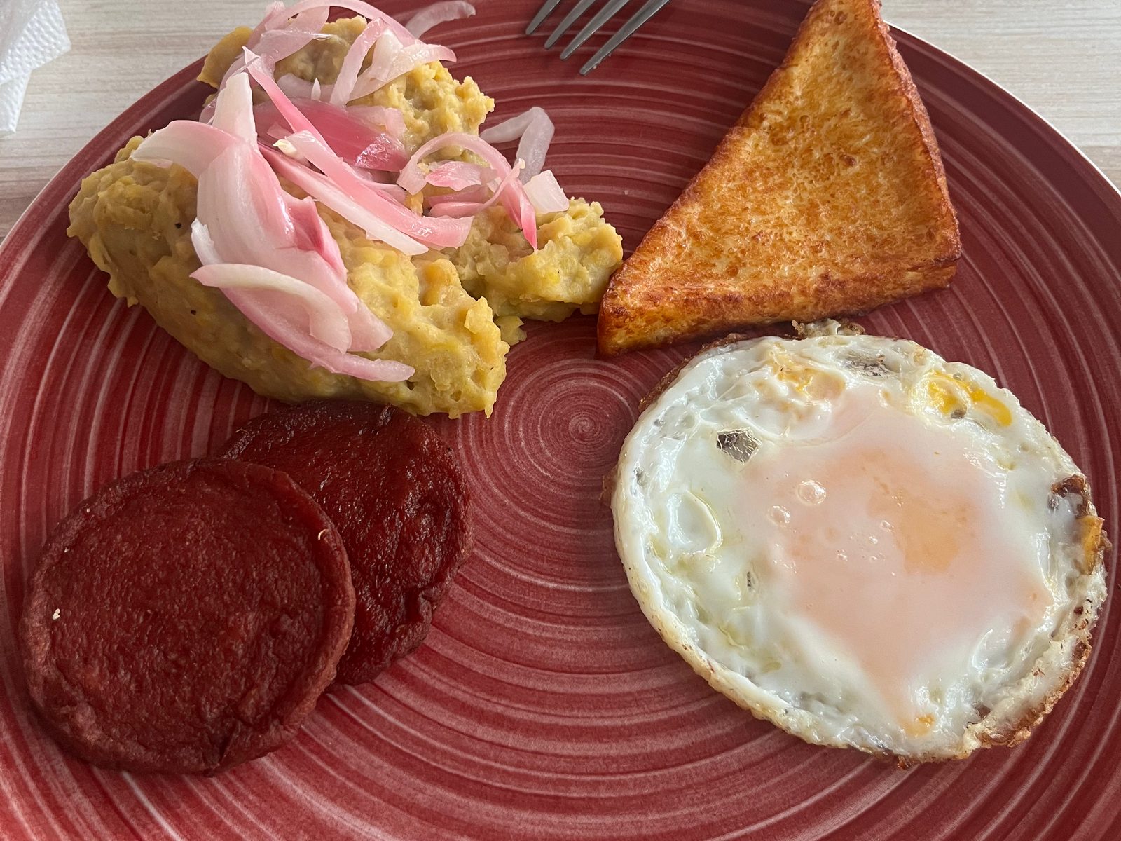 Breakfast plate with mangú topped with pickled onion, fried salami, a fried egg and toast