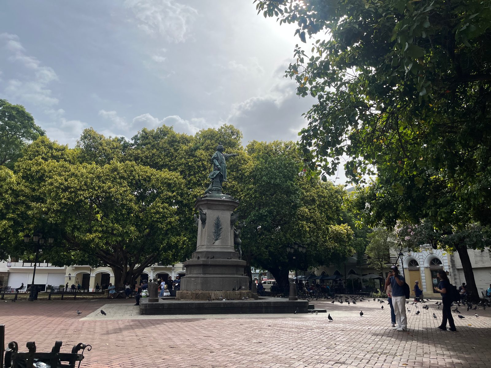 Parque Colón with the Columbus statue, shade trees and a few people crossing the square