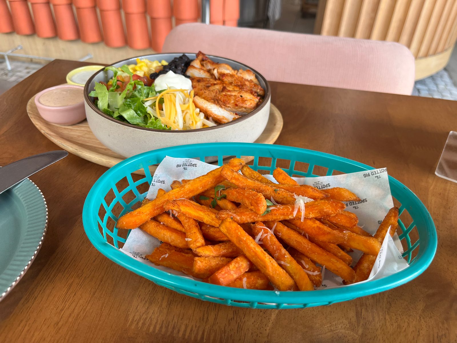 A salad bowl with grilled chicken, corn, black beans and cheese next to a basket of sweet potato fries